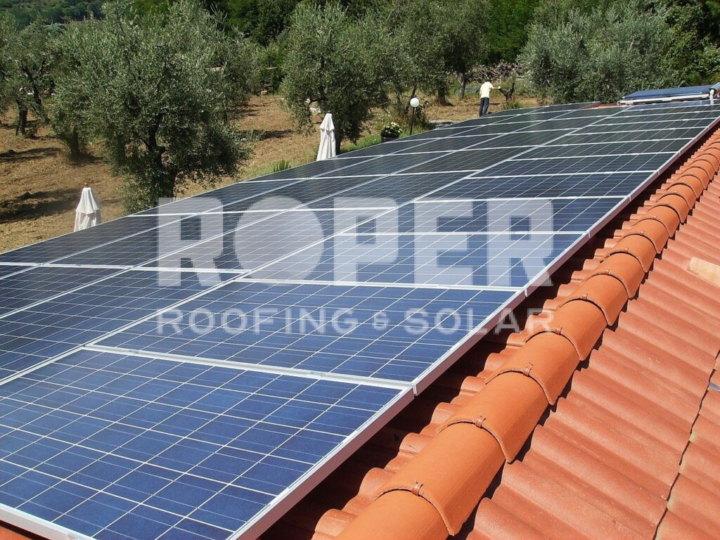 Solar panels installed on red tile roof with olive grove in background