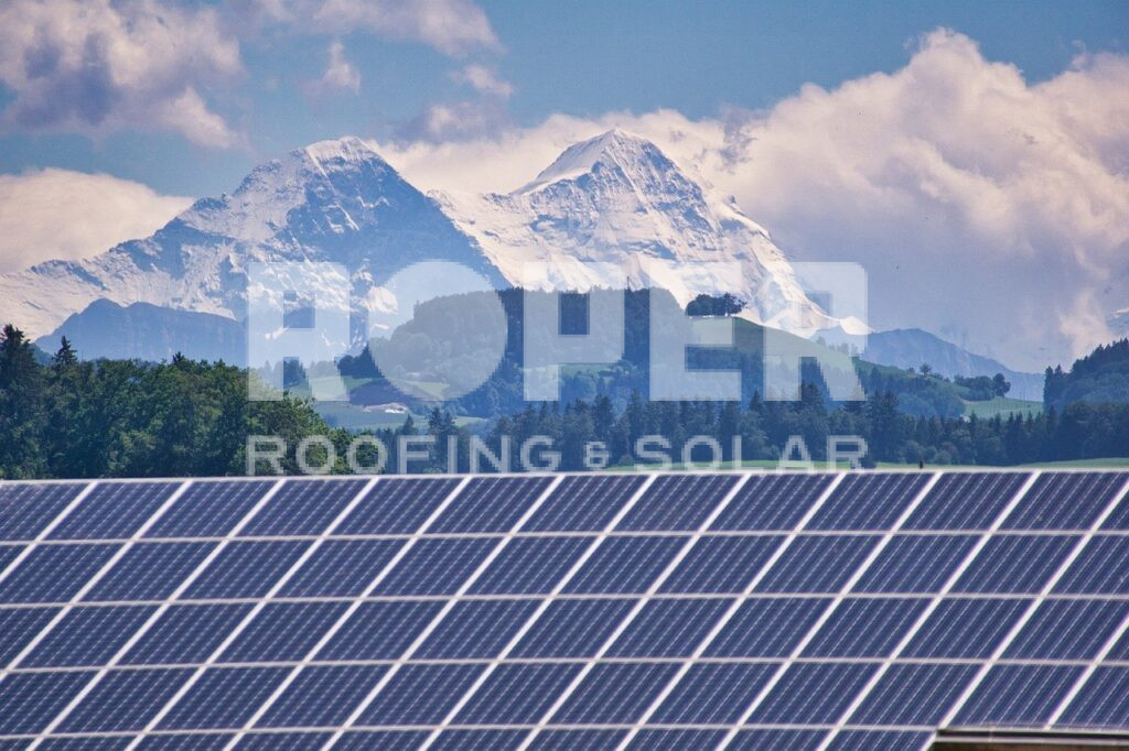 Solar panel farm with snow-capped mountains and cloudy sky in background