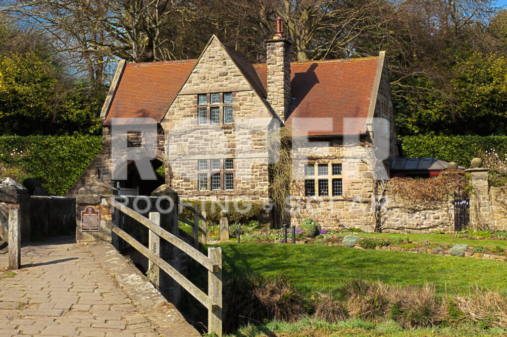 Historic stone mill building with orange tile roof and wooden bridge entrance