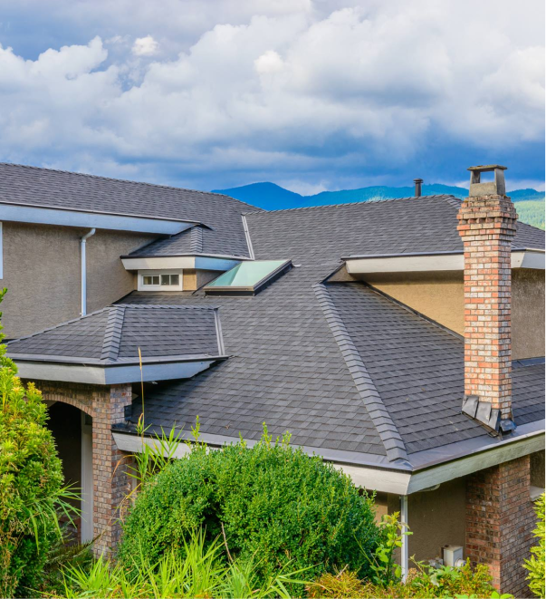 Modern residential house with dark gray shingle roof and brick chimney against mountain backdrop