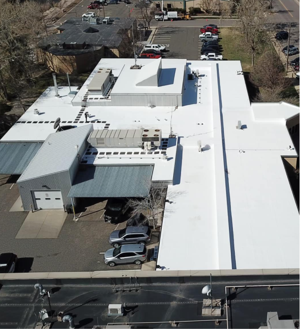 Aerial view of large industrial building with white roof and parking lot