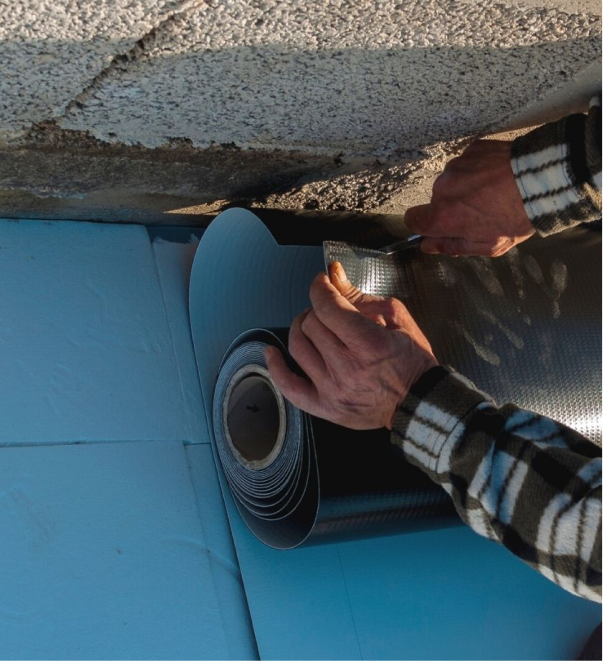 Worker installing waterproof membrane on concrete foundation for basement repair