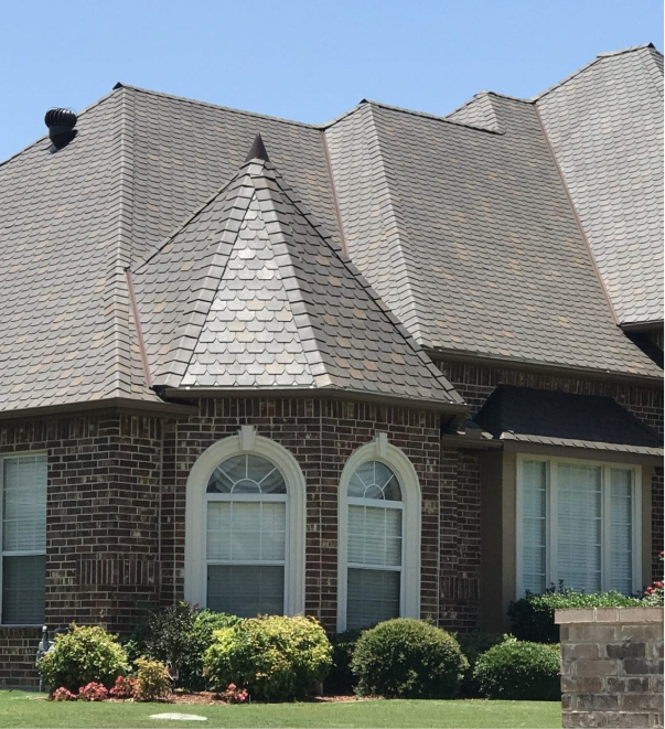Modern brick house with gray shingle roof and arched windows under blue sky