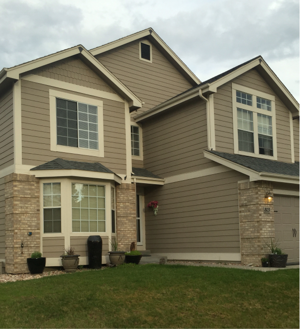 Modern two-story home with beige siding, brick accents, and bay window