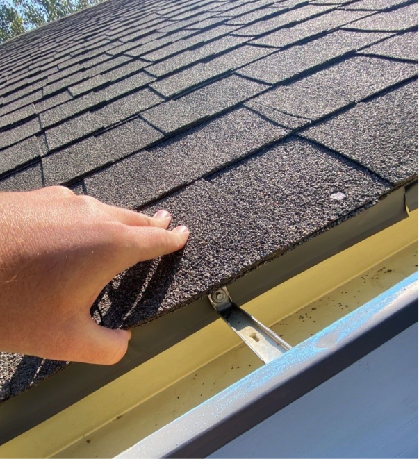 Hand lifting damaged asphalt roof shingle showing wear and tear on residential roof