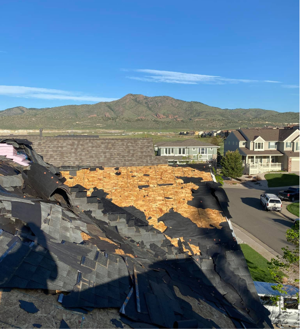 Damaged roof with torn shingles and exposed wood decking in suburban neighborhood