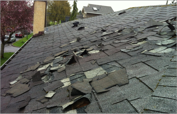 Severely damaged asphalt shingle roof with missing and broken shingles exposing decking