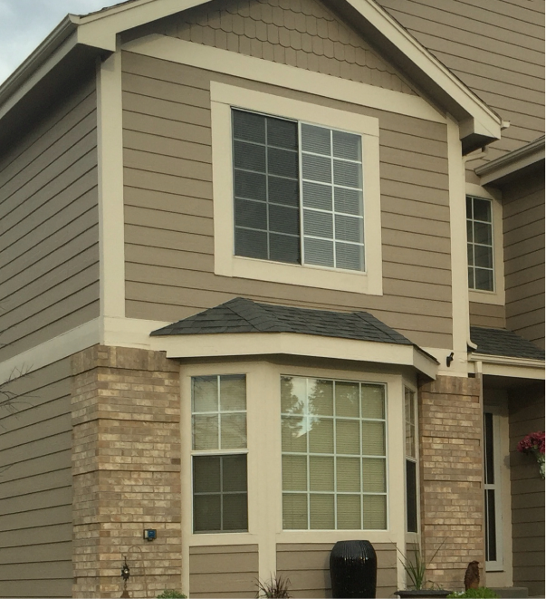 Modern two-story house with beige vinyl siding and brick accents featuring bay window
