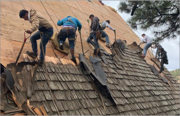 Construction workers removing old shingles and installing new plywood decking on house roof