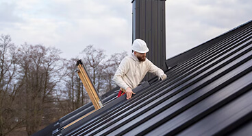 Professional roofer in white hard hat installing materials on dark metal roof