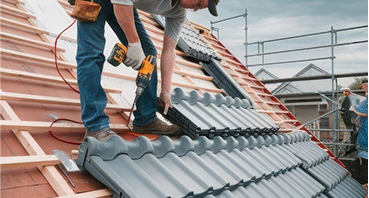 Construction workers installing gray corrugated metal roofing tiles on residential house