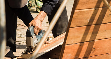 Carpenter using hammer to build wooden deck structure outdoors in sunlight