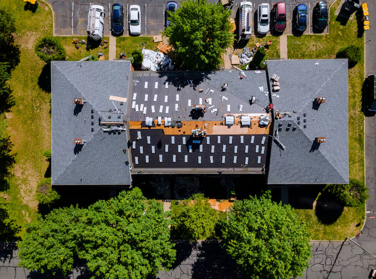 Aerial view of roofing construction work on gray shingled roof with workers and materials
