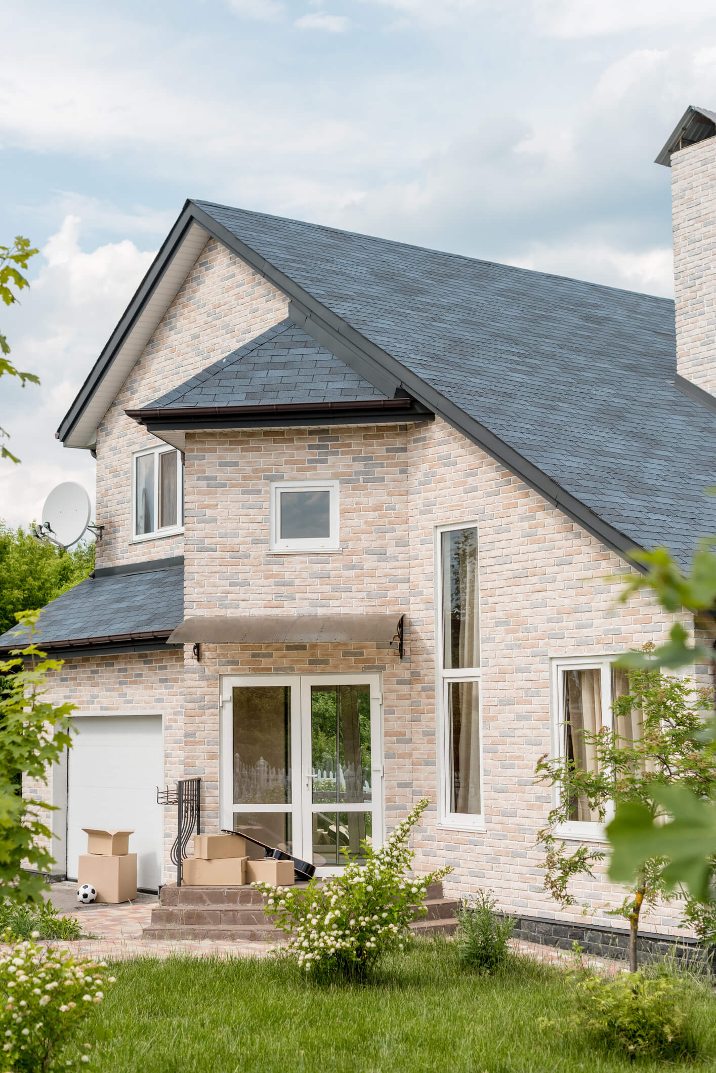 Modern brick house with gray slate roof and moving boxes on front porch steps