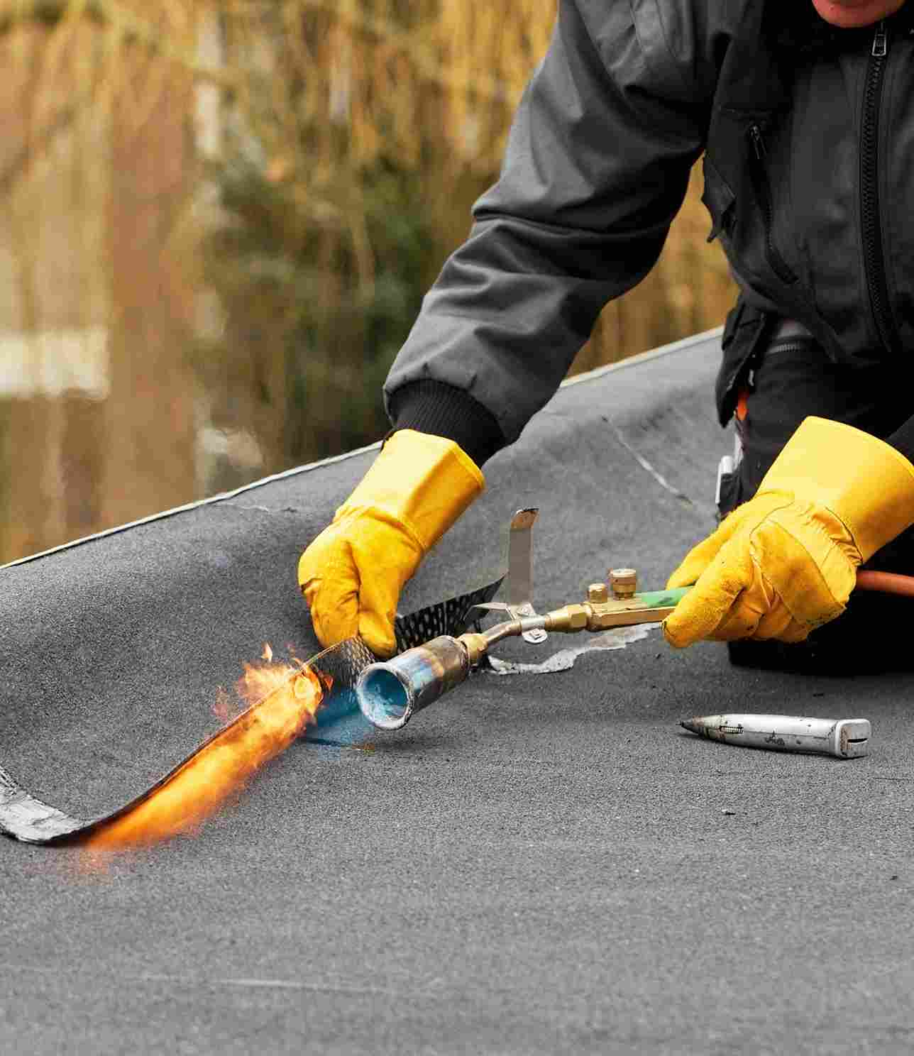 Roofer using torch to install waterproof membrane on flat roof surface