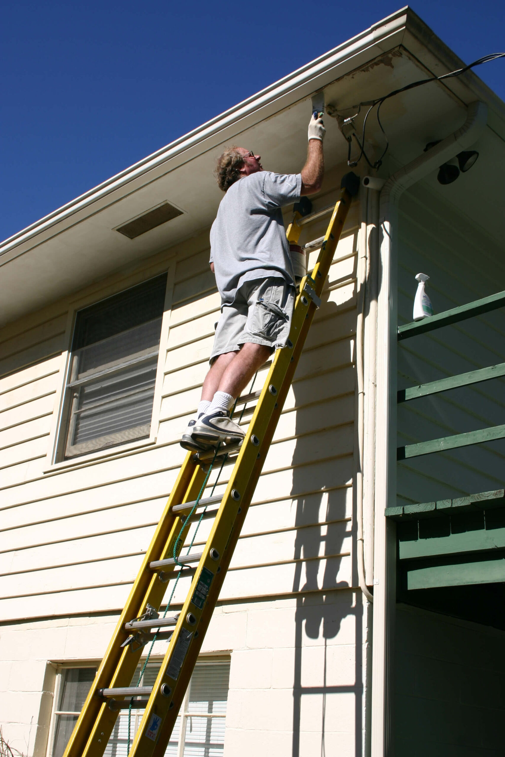 Man on yellow ladder working on house exterior maintenance repair project