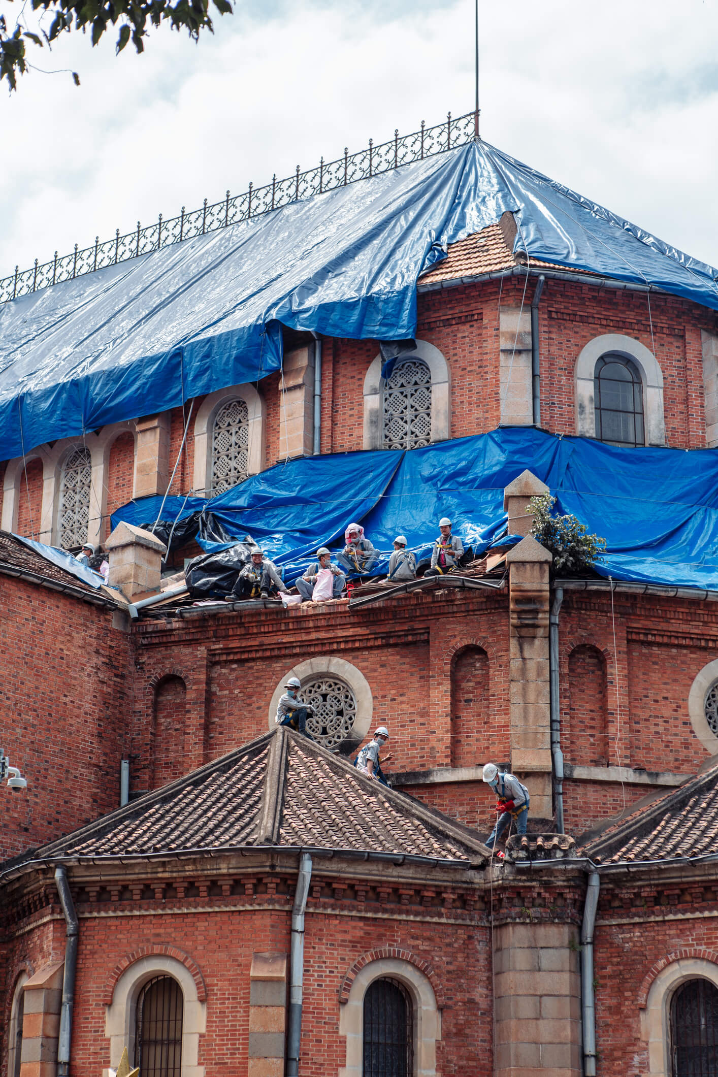 Construction workers repairing historic brick church roof covered with blue tarp