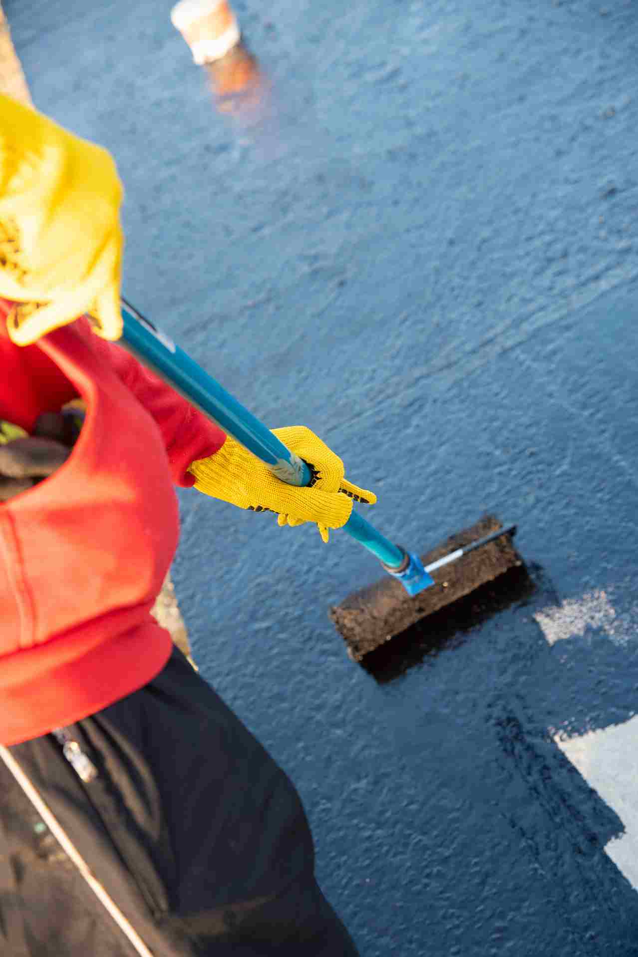 Worker in yellow gloves using scraper tool to remove old flooring material