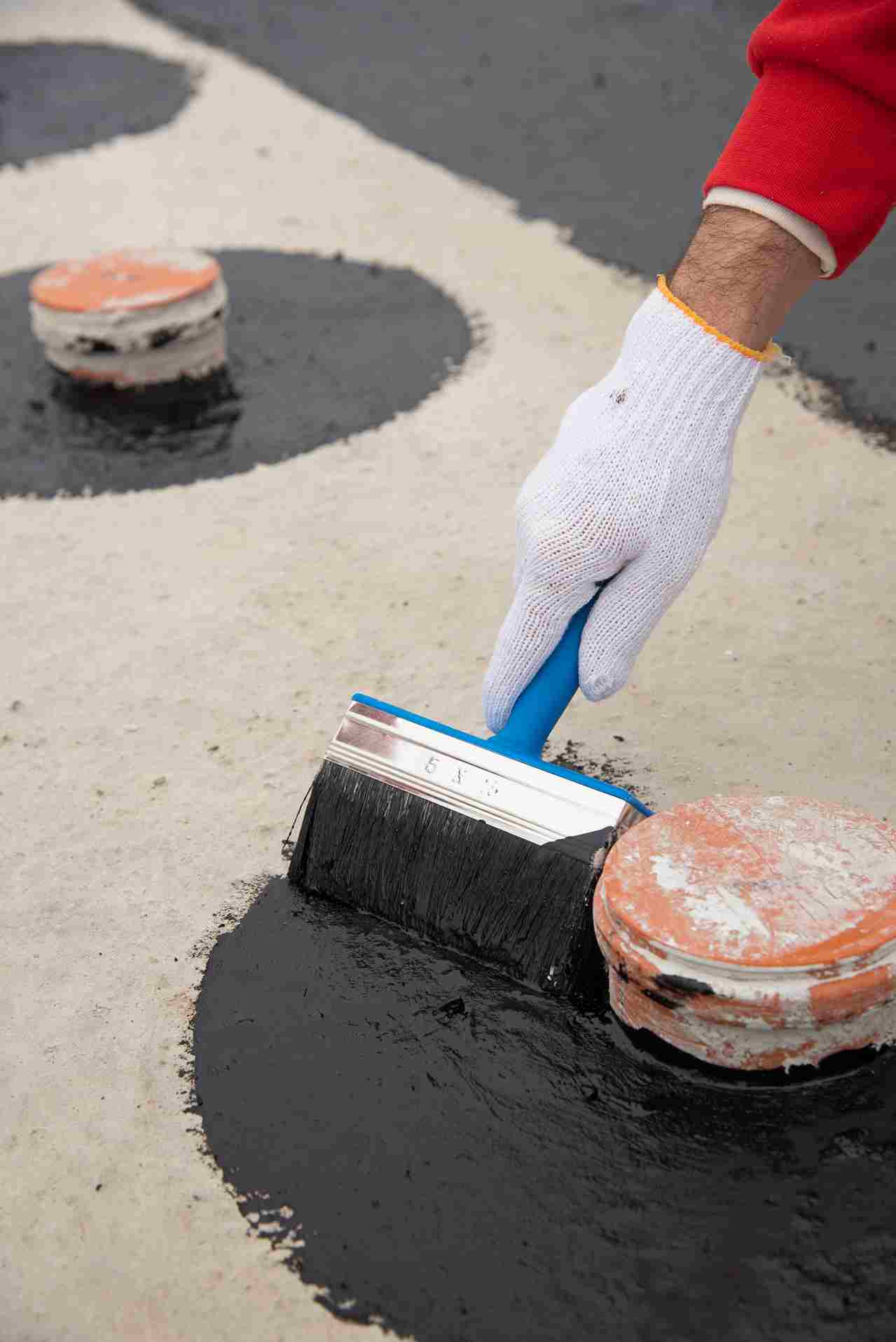 Worker applying black waterproof coating with brush on concrete surface