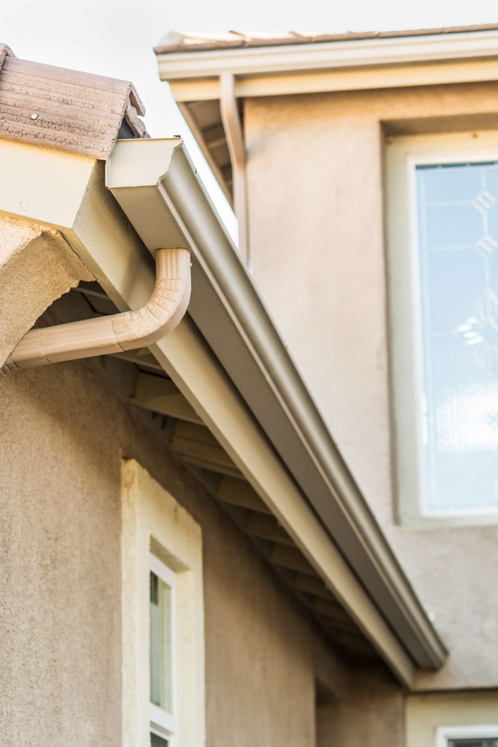 Beige rain gutters and downspouts on residential home exterior with tile roof