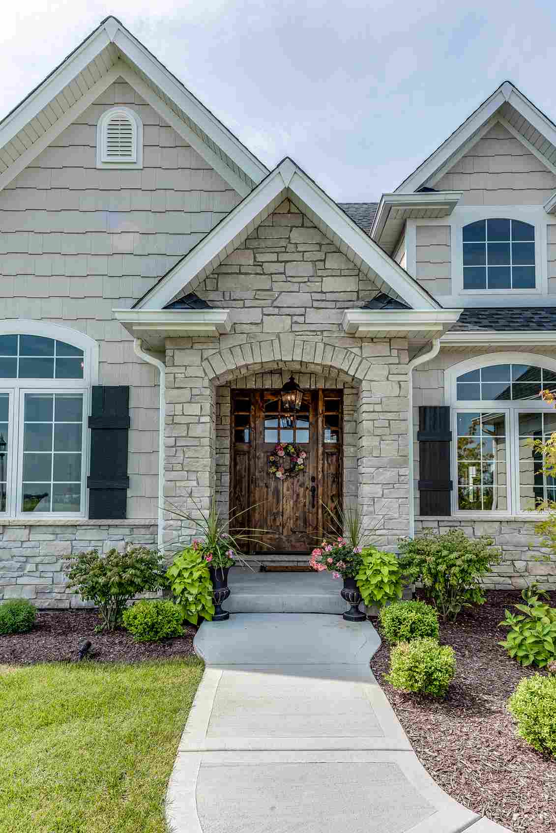 Elegant stone and shingle home exterior with arched wooden front door and landscaping