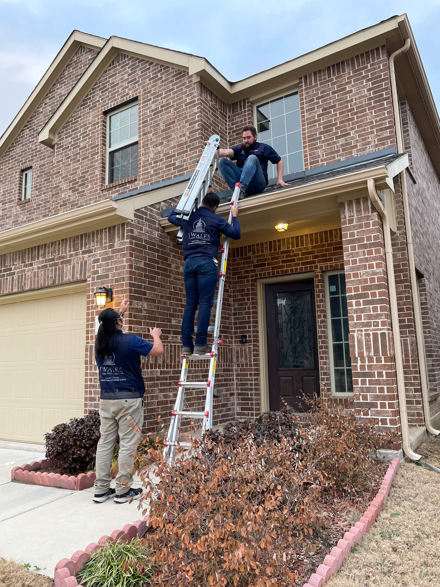 Professional home inspectors using ladder to examine brick house exterior and roof