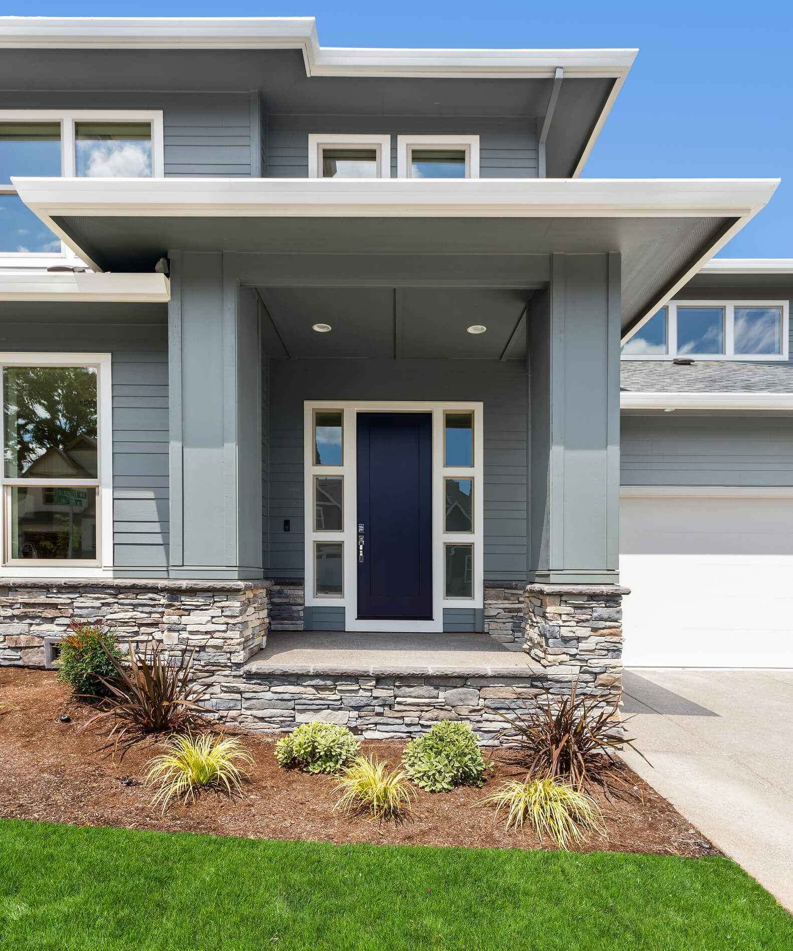 Modern gray house exterior with blue front door, stone accents, and landscaping