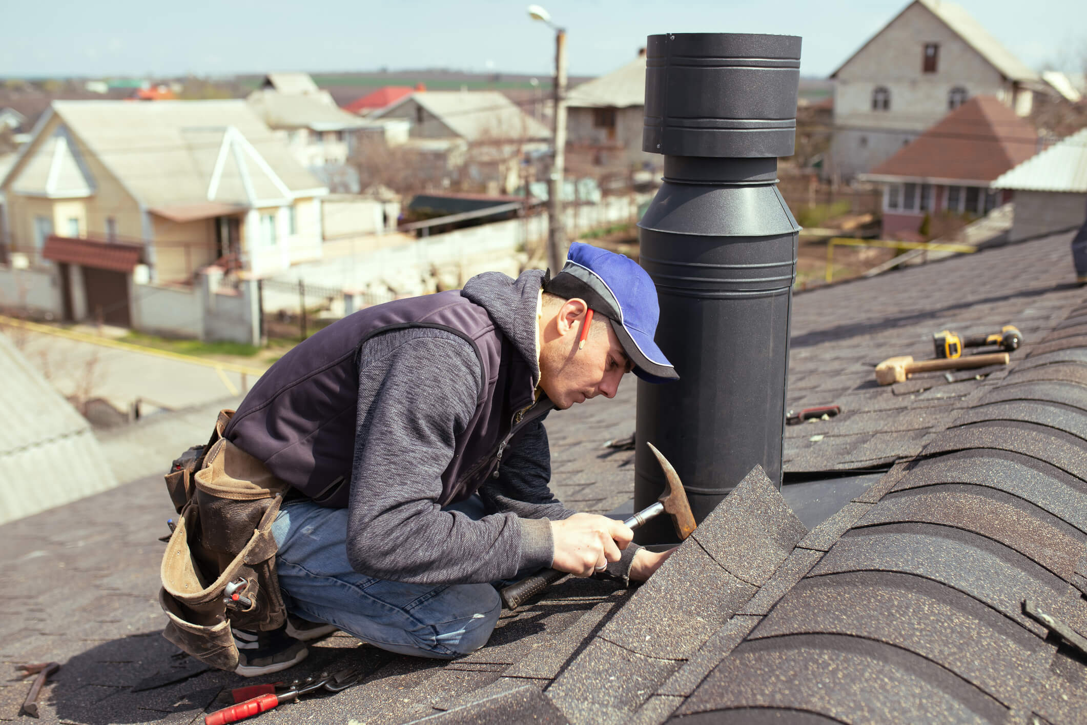 Roofer installing chimney pipe on residential roof with hammer and tools