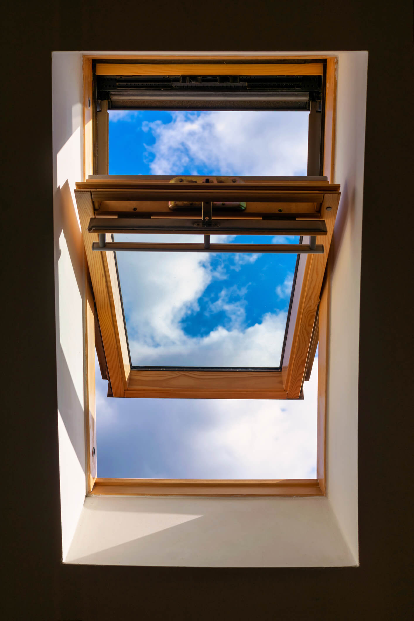 Open wooden skylight window showing blue sky with white clouds from interior view