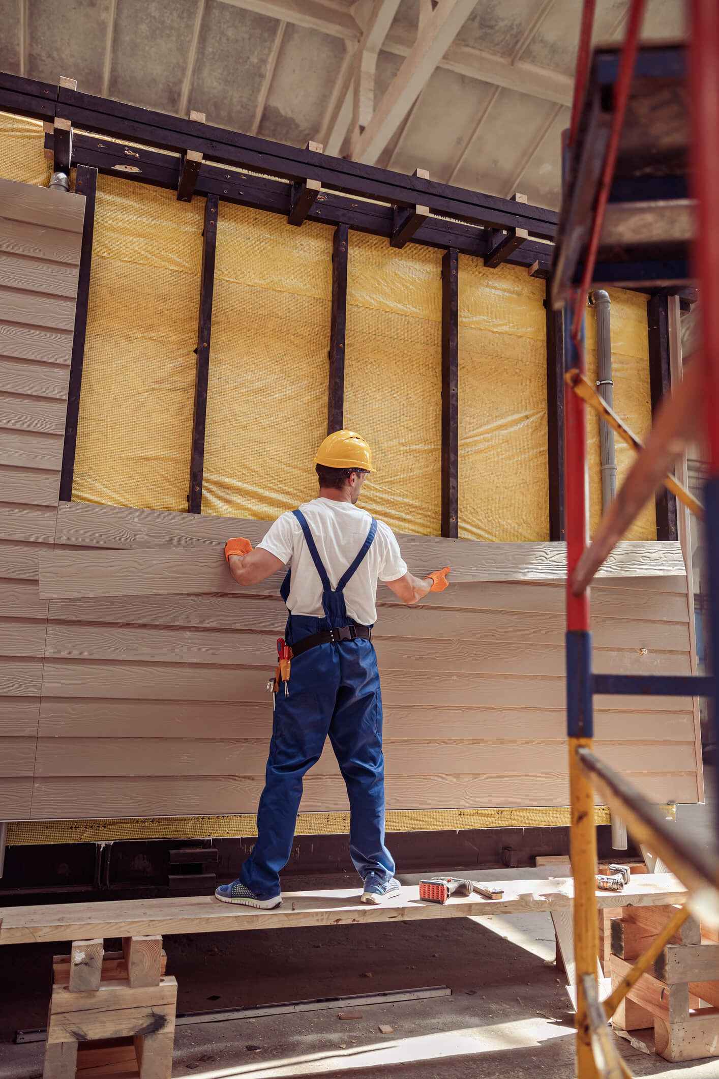 Construction worker installing yellow insulation in wooden frame house structure