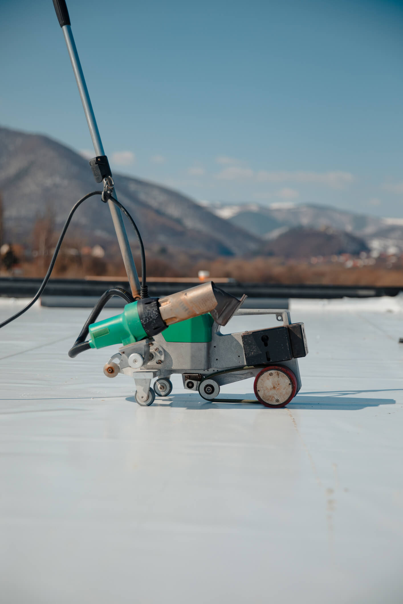 Roof welding equipment with green tank on white membrane against mountain backdrop