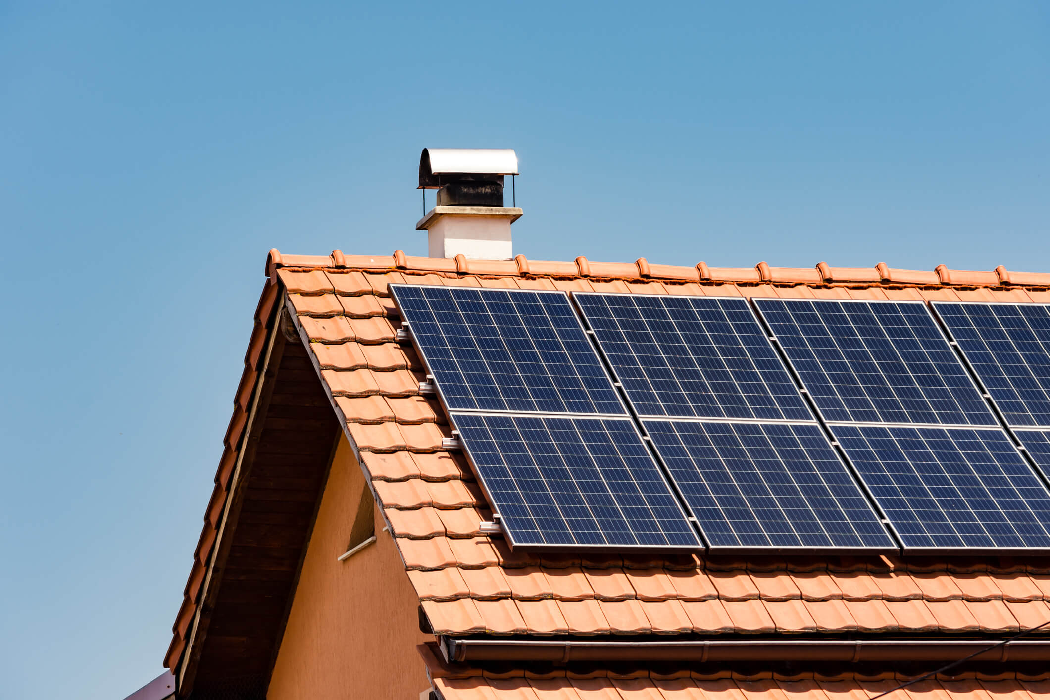 Solar panels installed on red tile roof with chimney against clear blue sky