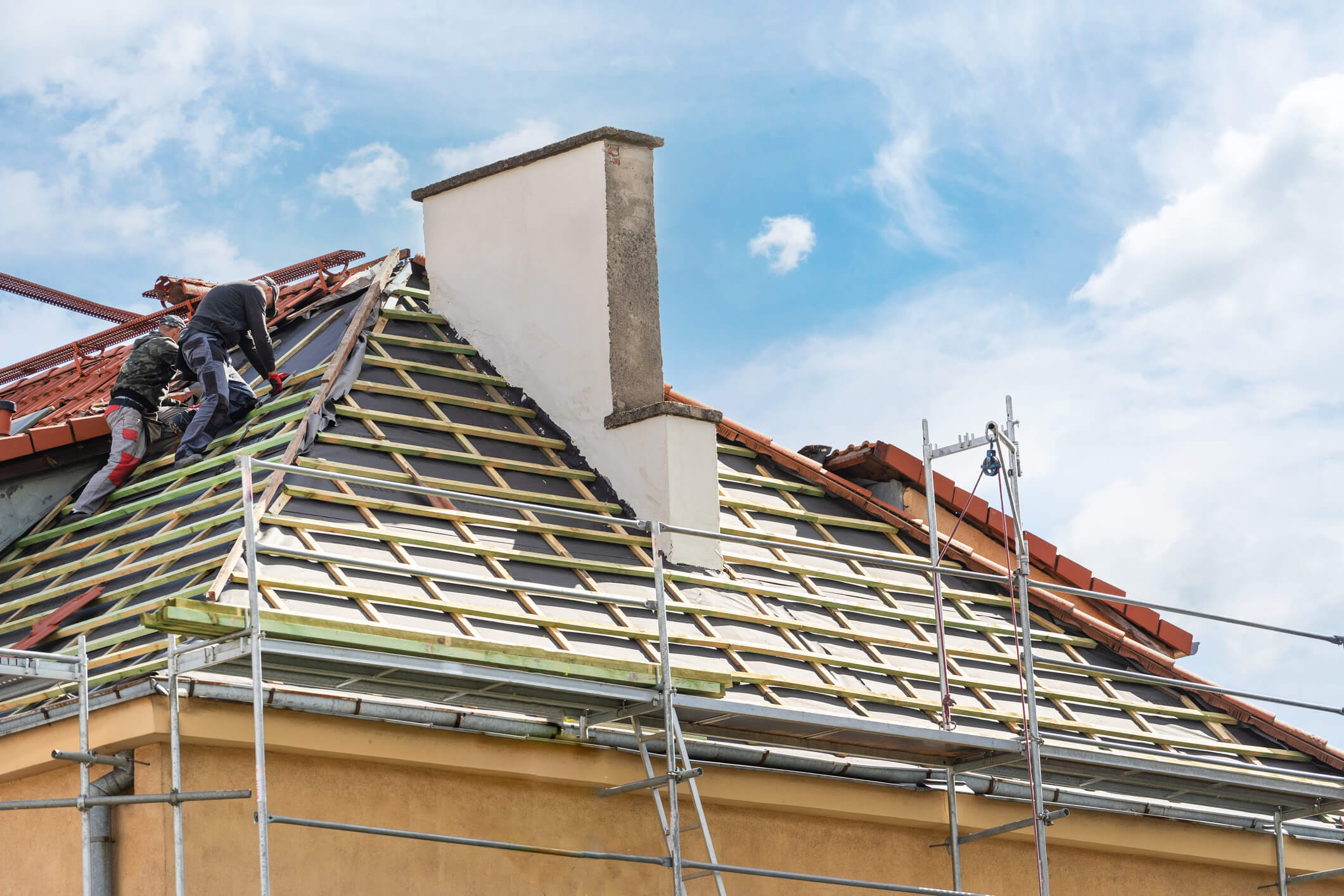 Roofer installing red clay tiles on house roof with scaffolding under blue sky