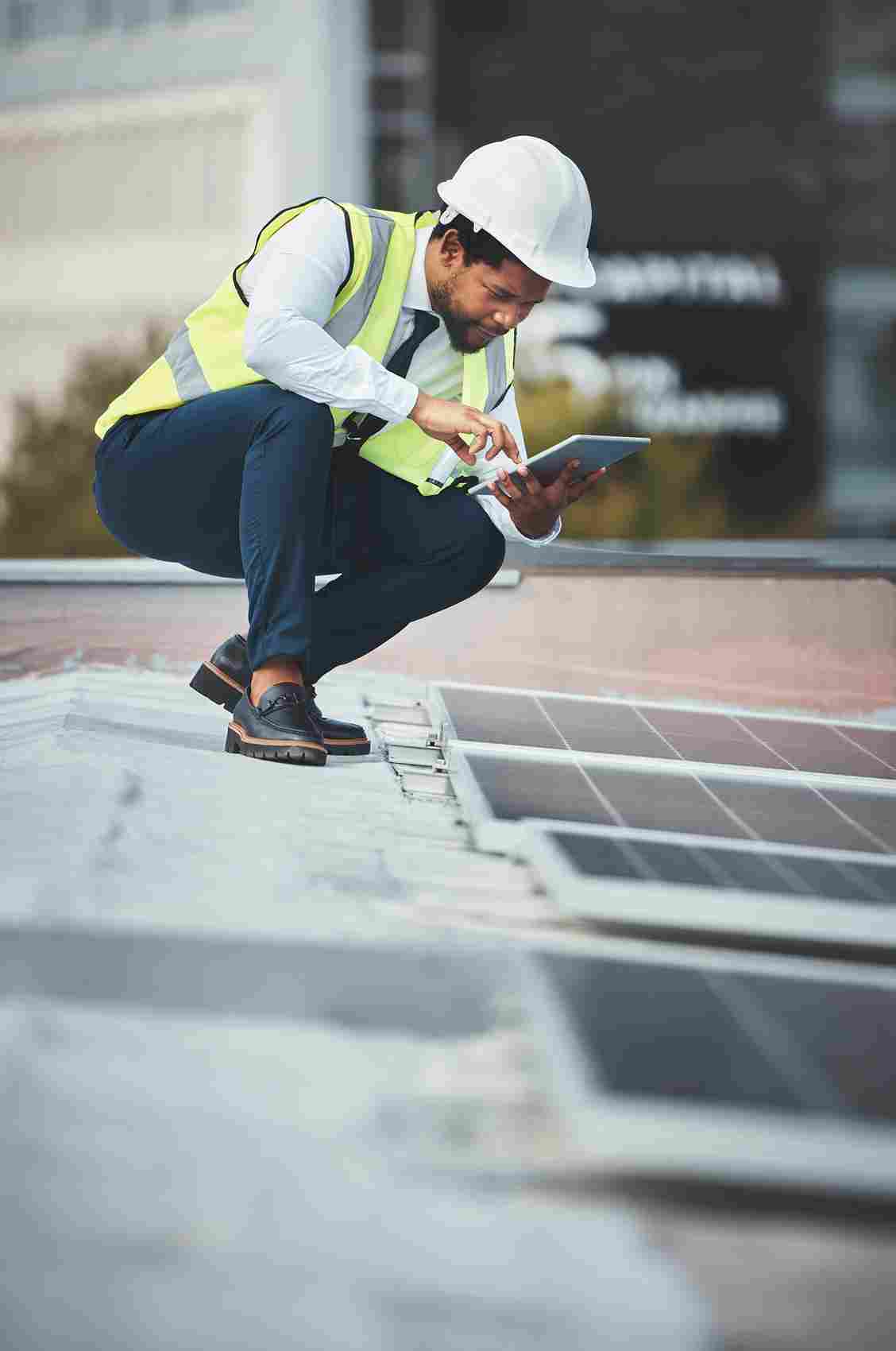 Construction worker in hard hat and safety vest using tablet on solar panel roof