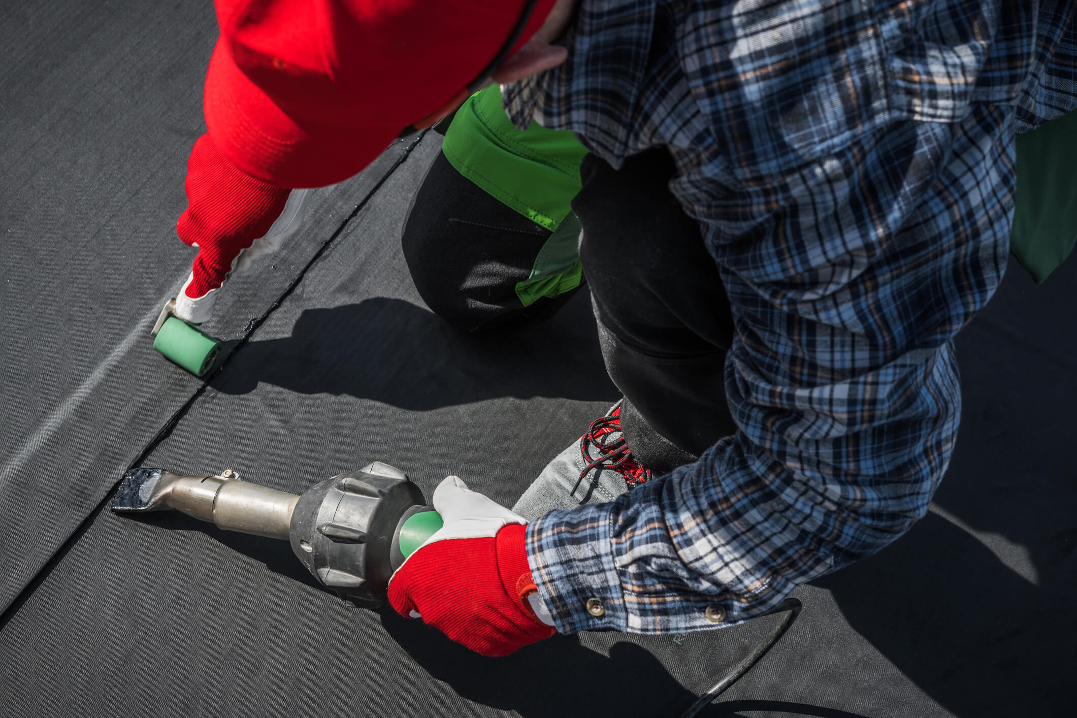 Worker in red gloves using green caulk gun on roofing shingles for repair work