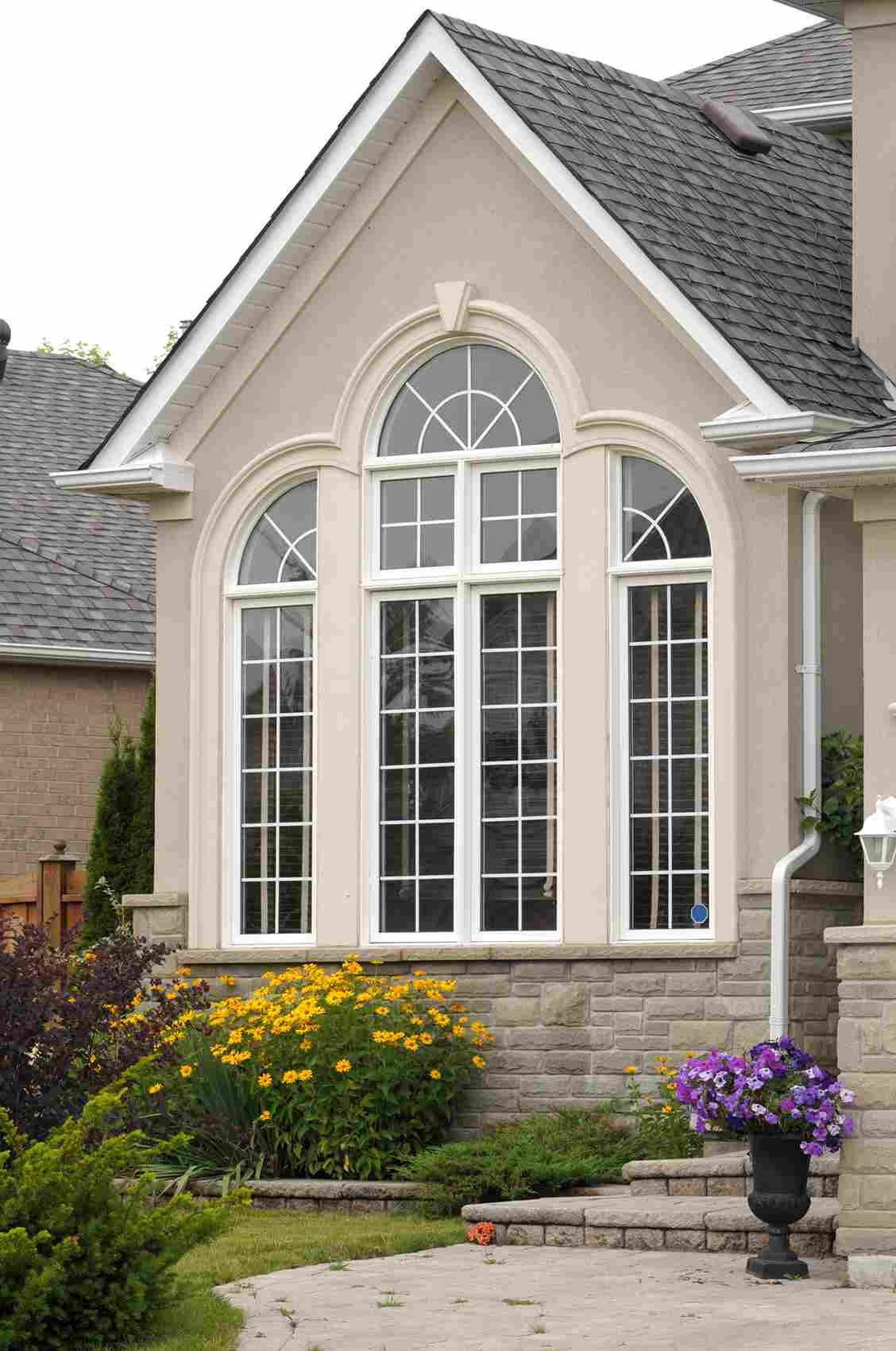 Elegant arched windows with white trim on beige house exterior with landscaping