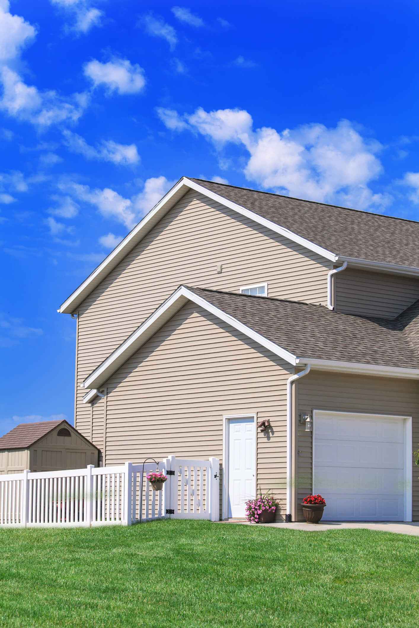 Beige vinyl siding house with white garage door and fence under blue sky