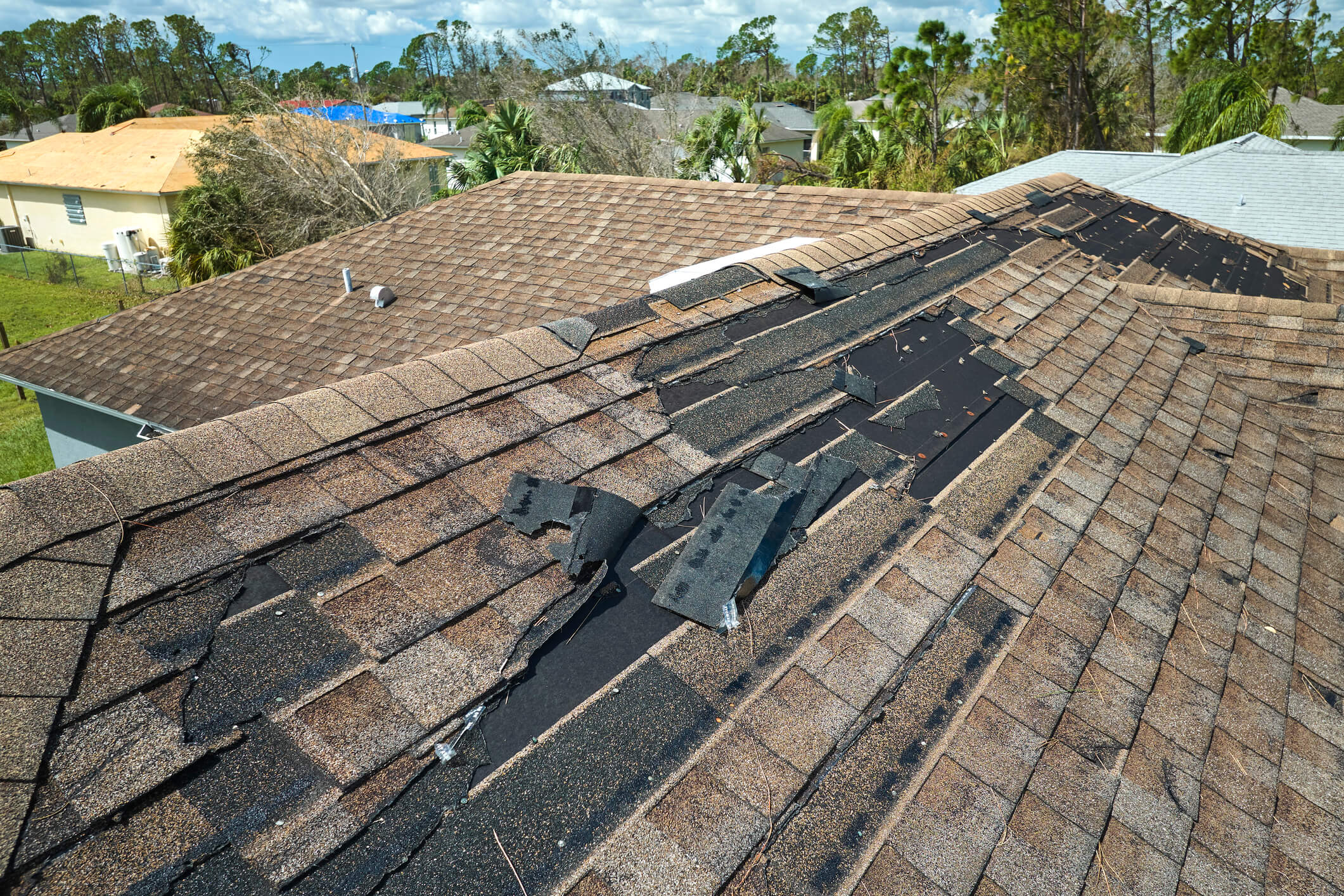 Storm damaged residential roof with missing shingles and exposed underlayment