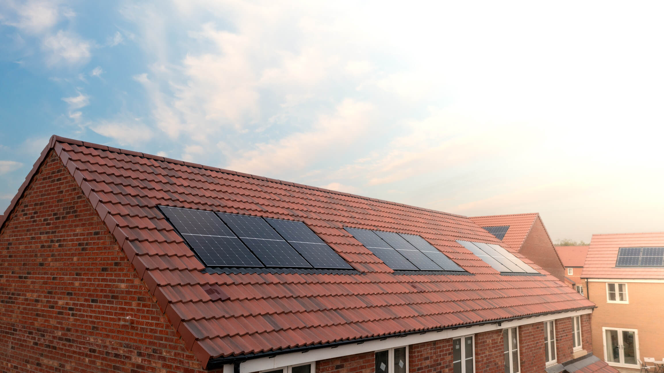 Solar panels installed on red tile roof of modern brick residential house