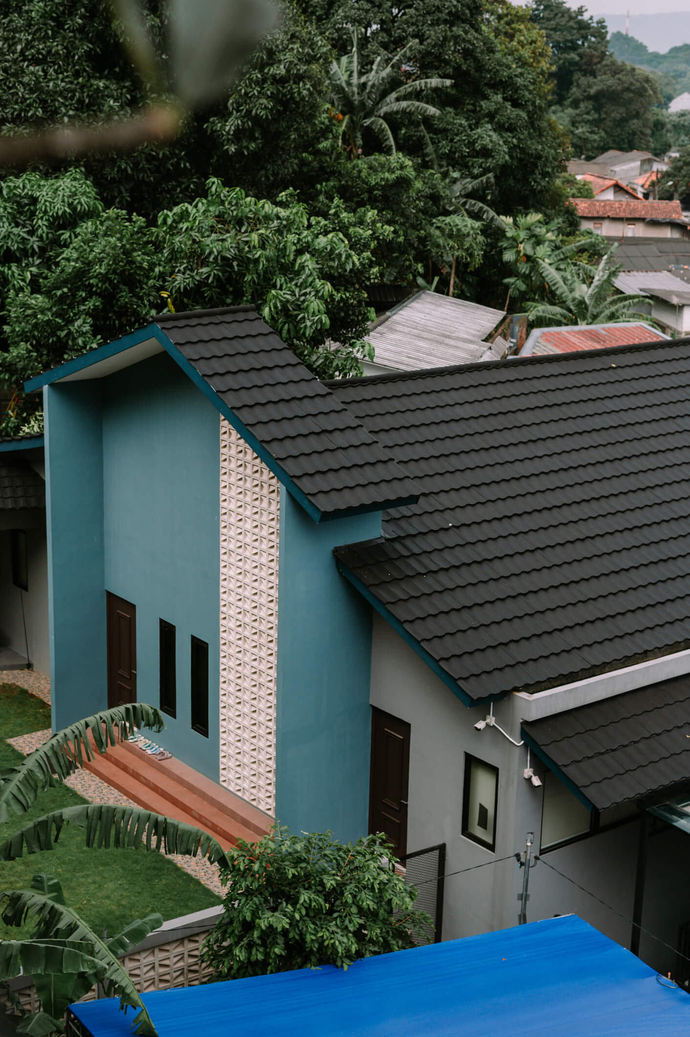 Modern blue and white house with dark tile roof surrounded by lush tropical trees