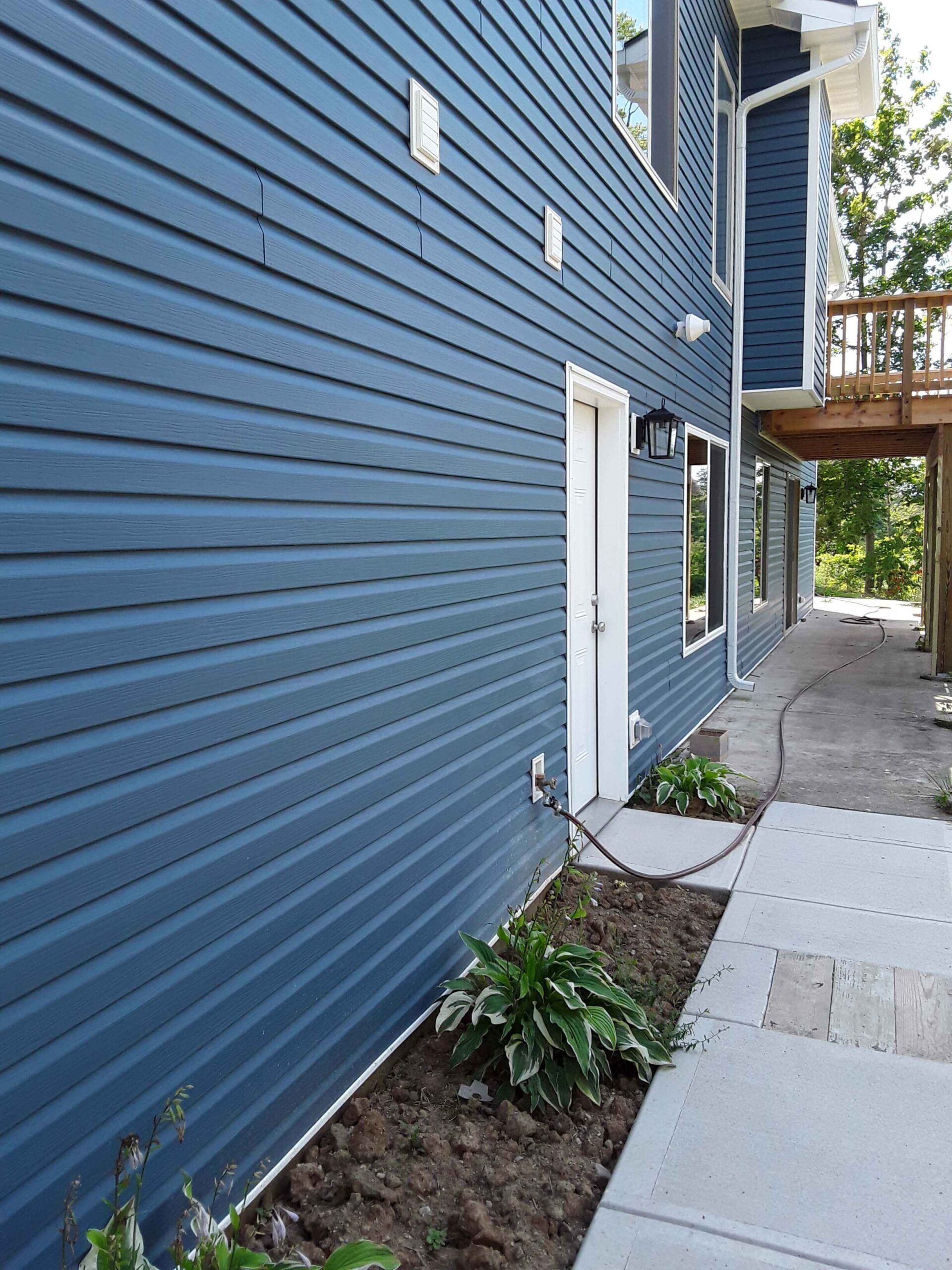 Blue vinyl siding house exterior with white door and concrete walkway