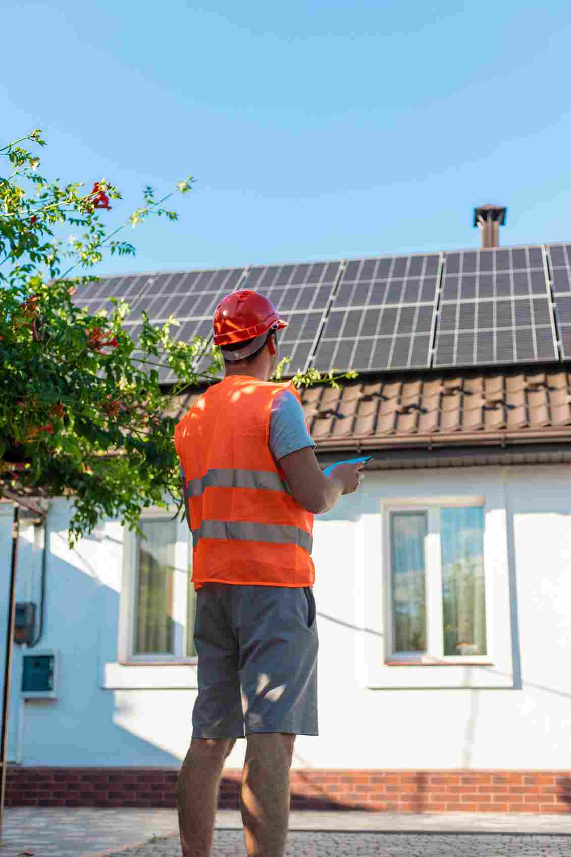 Solar panel installer in safety vest inspecting residential rooftop installation