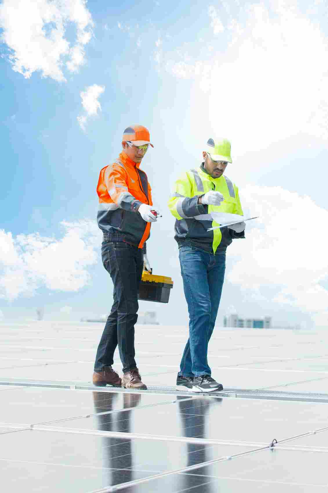 Two construction workers in safety gear reviewing documents on solar panel installation site