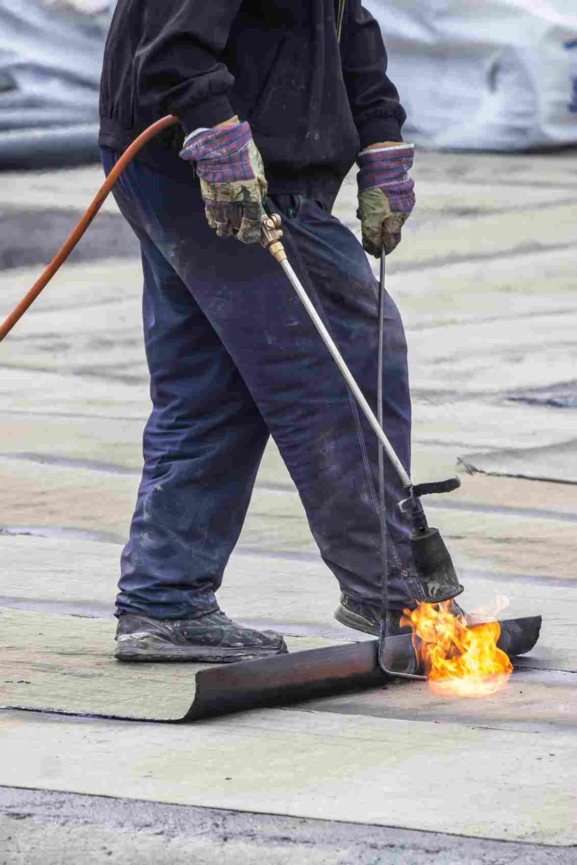 Worker using torch flame to seal waterproof membrane on concrete roof surface