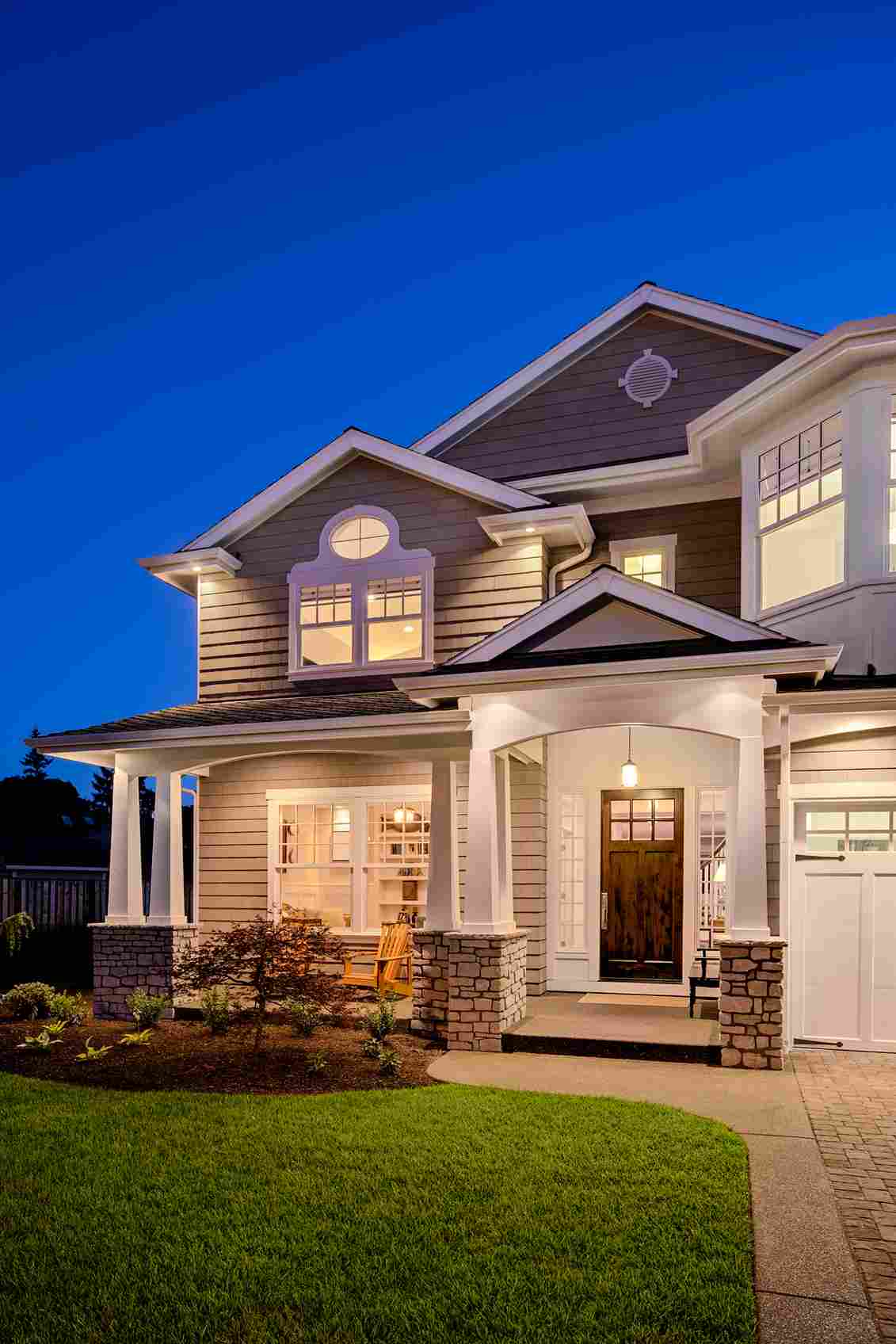 Beautiful two-story home with stone and siding exterior at twilight with lights on