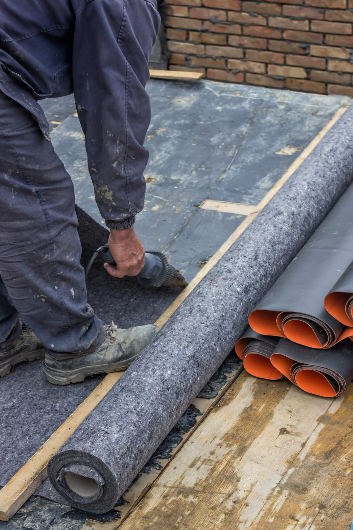 Construction worker installing waterproof membrane roofing material on building