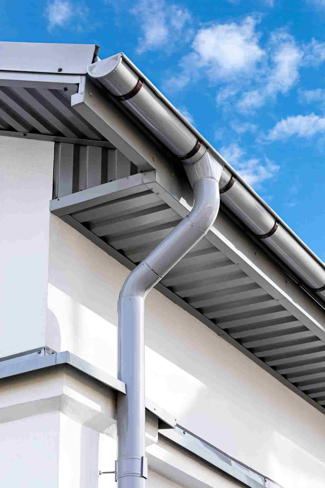 White metal gutters and downspout on modern house roof against blue cloudy sky