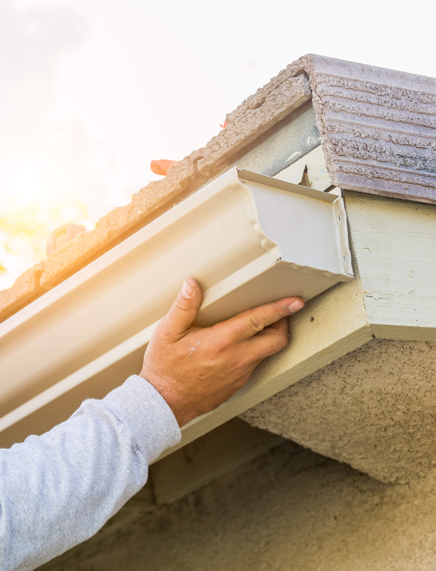Worker installing white gutter system on residential roof with tile shingles