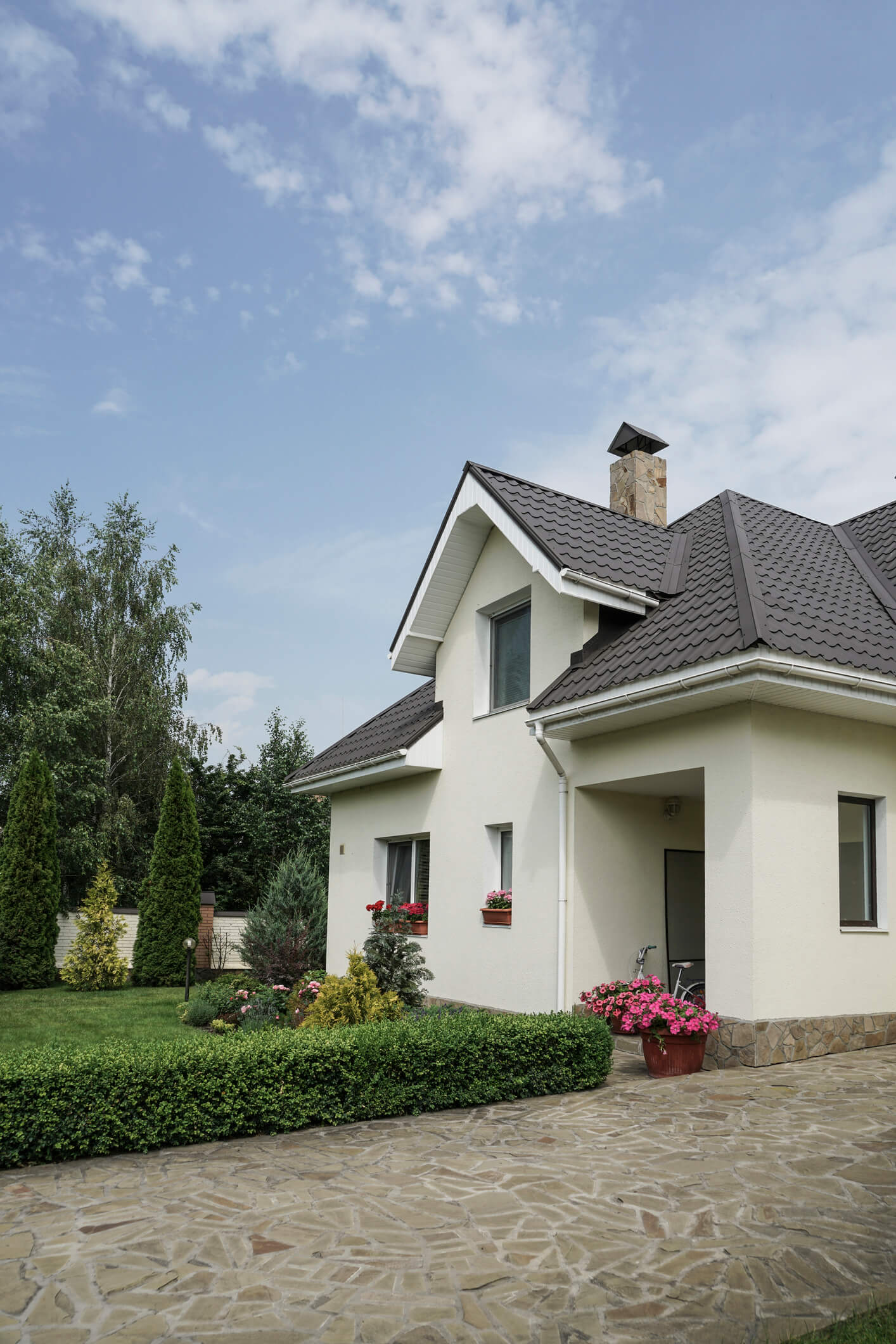 Modern white house with gray tile roof and stone chimney surrounded by landscaped garden