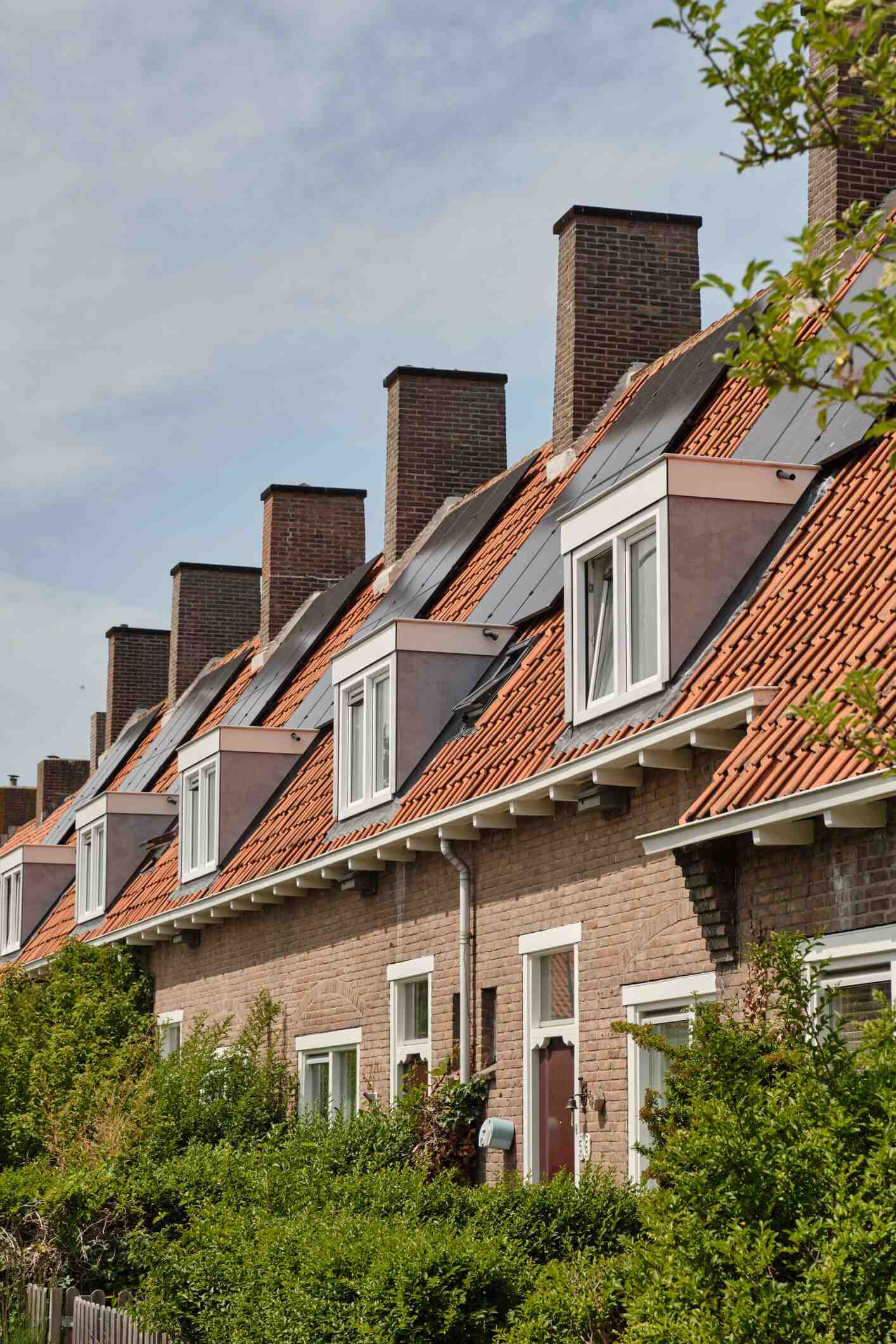 Row of brick houses with red tile roofs, dormer windows and tall chimneys